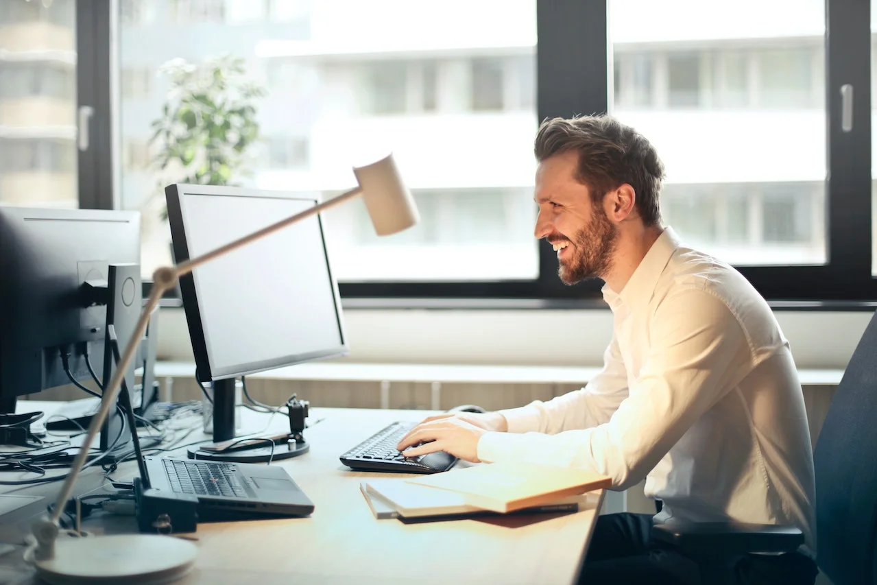 Unternehmer lächelnd vor dem Bildschirm in einem Büro Mann lächelnd vor dem Bildschirm in einem Büro