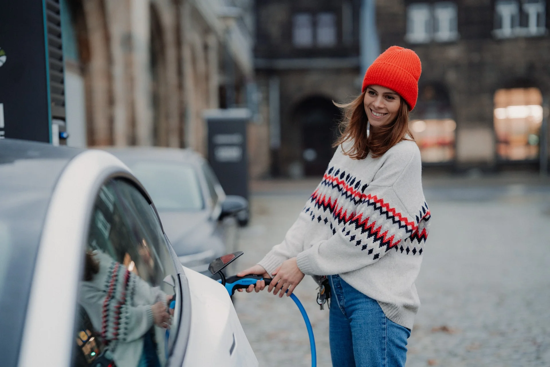 women in bright red hat smiling while charging her electronic vehicle