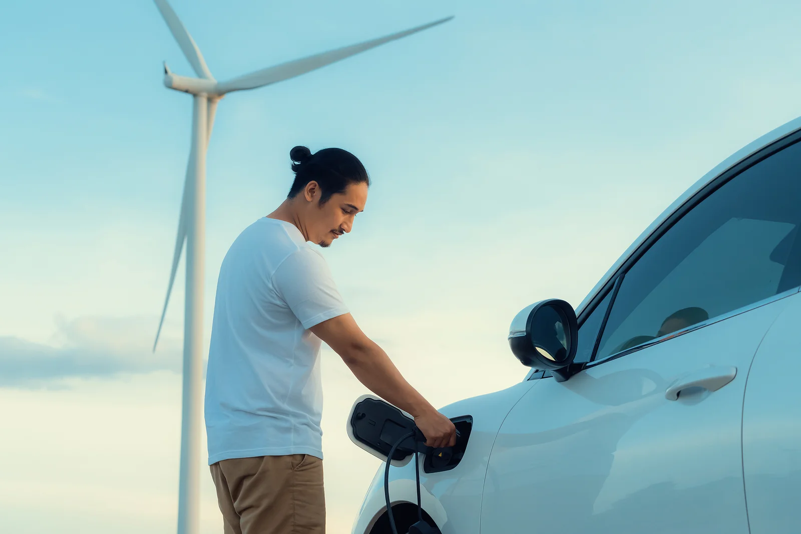 Un hombre carga su coche eléctrico con la energía de un aerogenerador