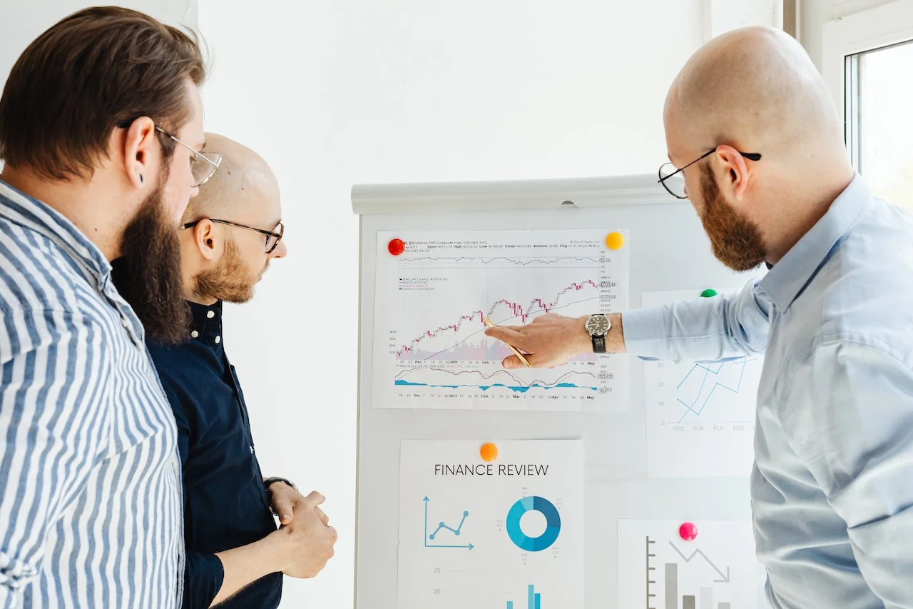 3 Männer diskutieren Chancen durch steigende Verkaufszahlen im Rahmen einer SWOT-Analyse 3 Männer schauen auf einen ausgedruckten Graphen auf einem Whiteboard