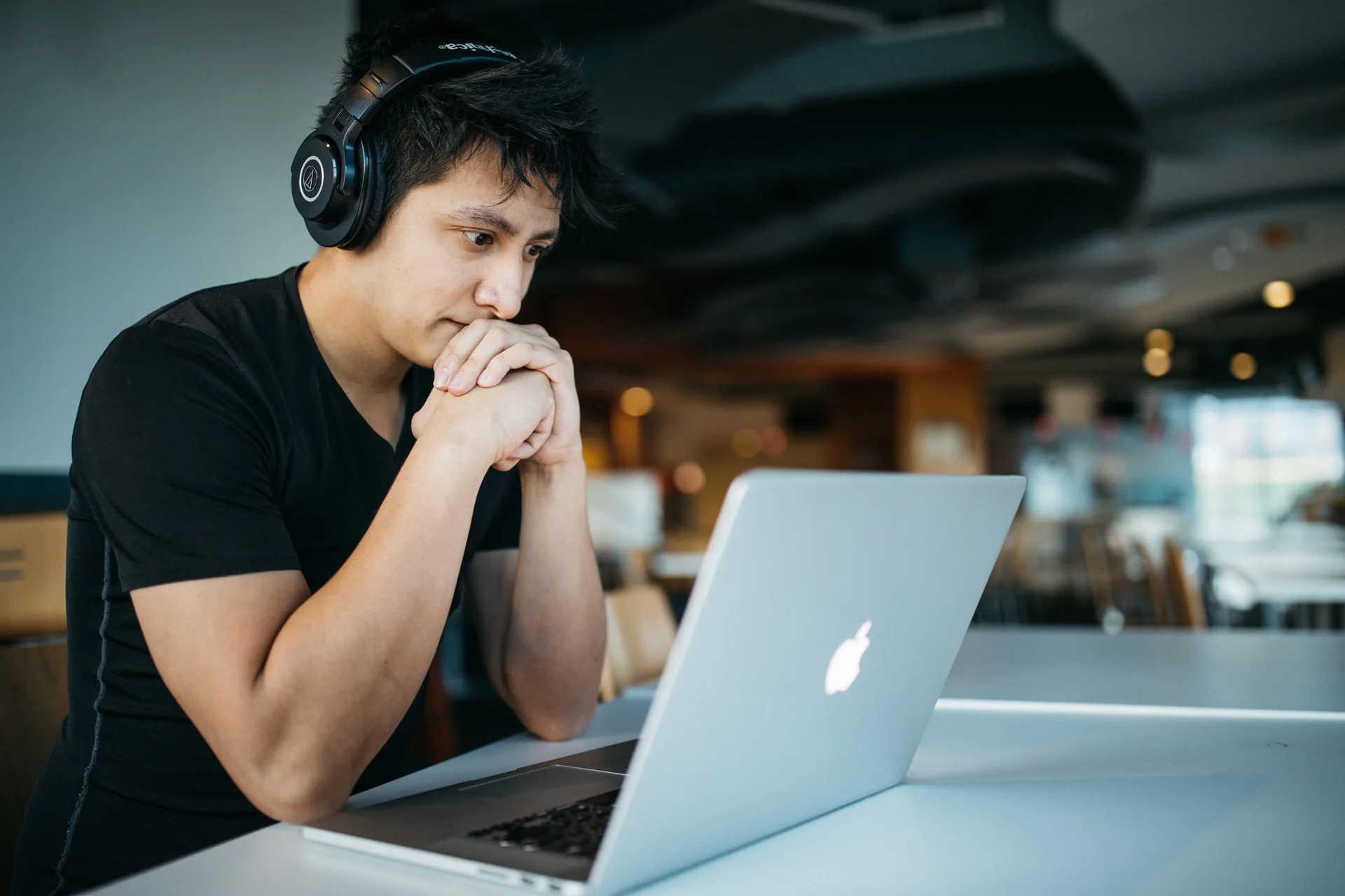 Desktop-ISO-Audit, das von einem jungen Mitarbeiter aus der Ferne durchgeführt wird Ein junger Mann sitzt mit Headset vor einem Apple Laptop