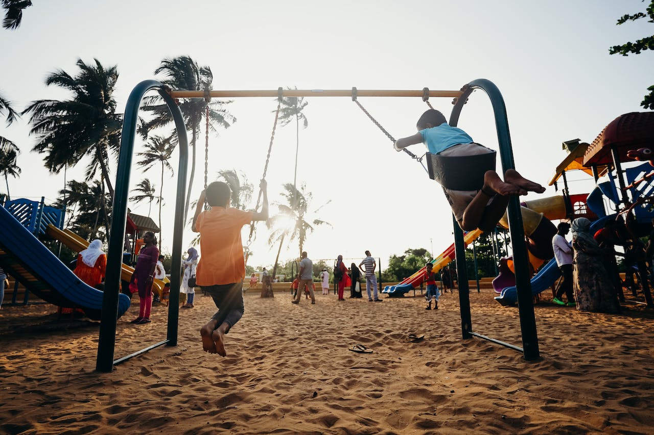 duas crianças no balanço do playground em momento de pôr-do-sol
