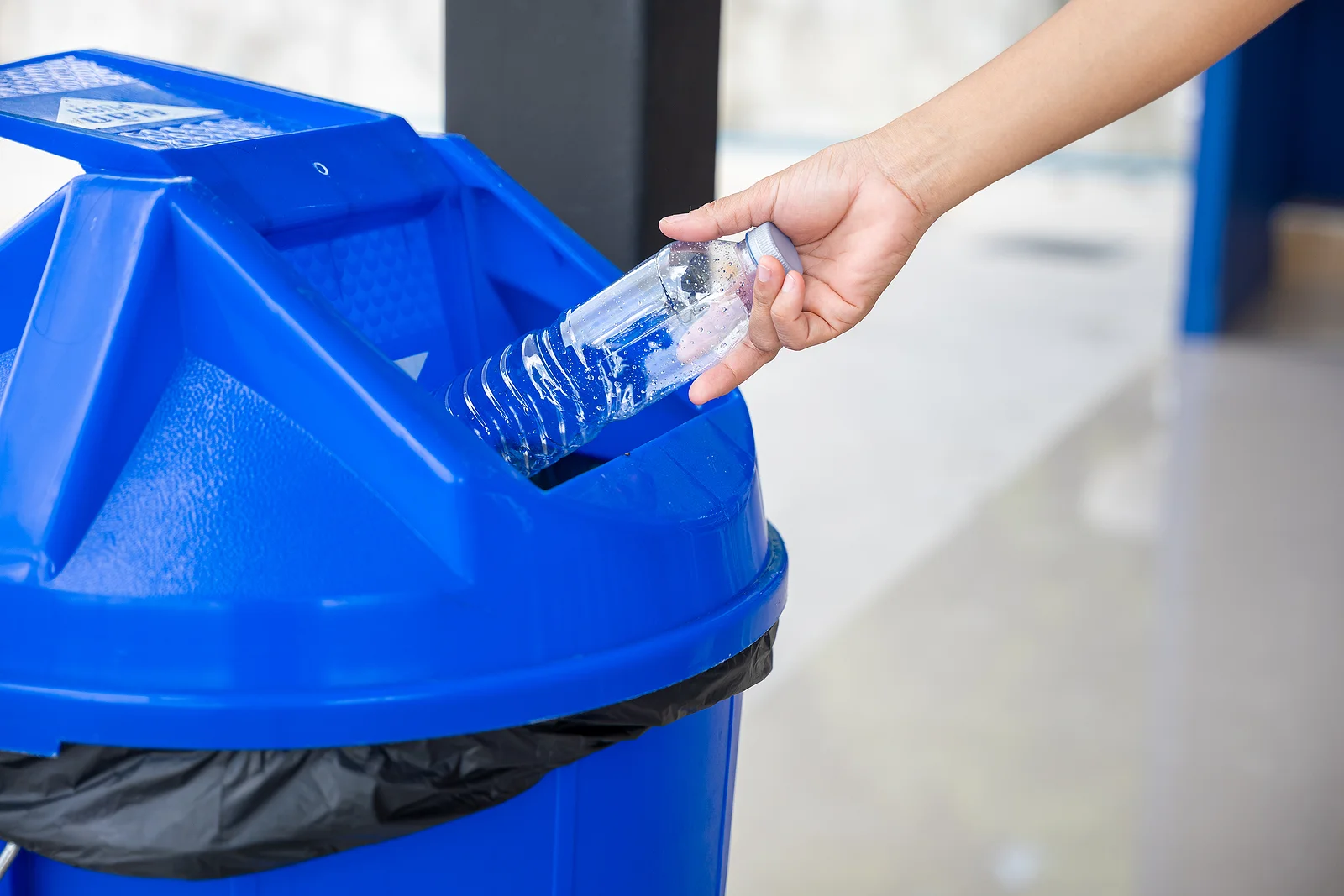 person recycling plastic water bottle in blue bin