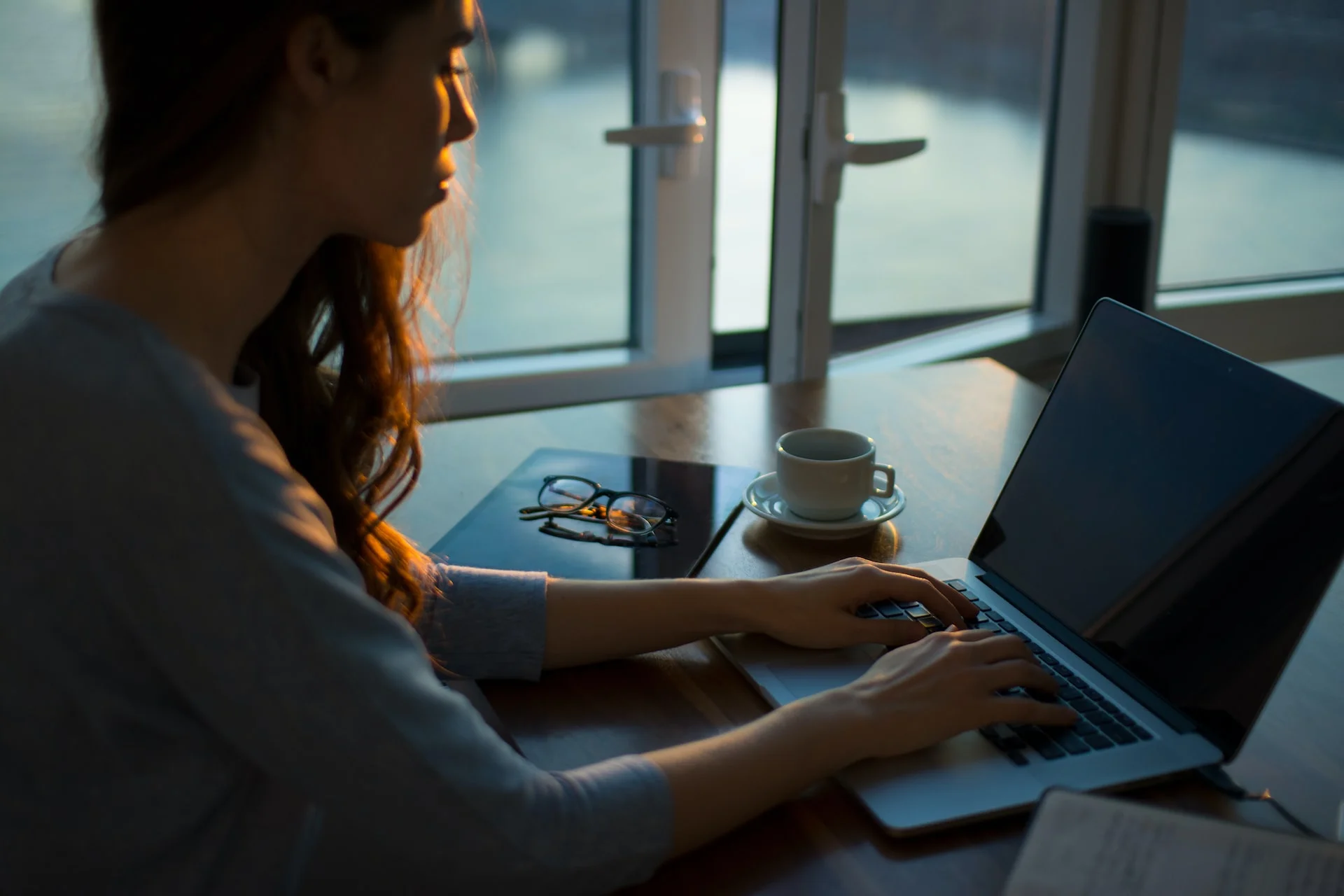 woman sitting at a desk with a notebook and coffee cup working on laptop woman sitting at a desk with a notebook and coffee cup working on laptop